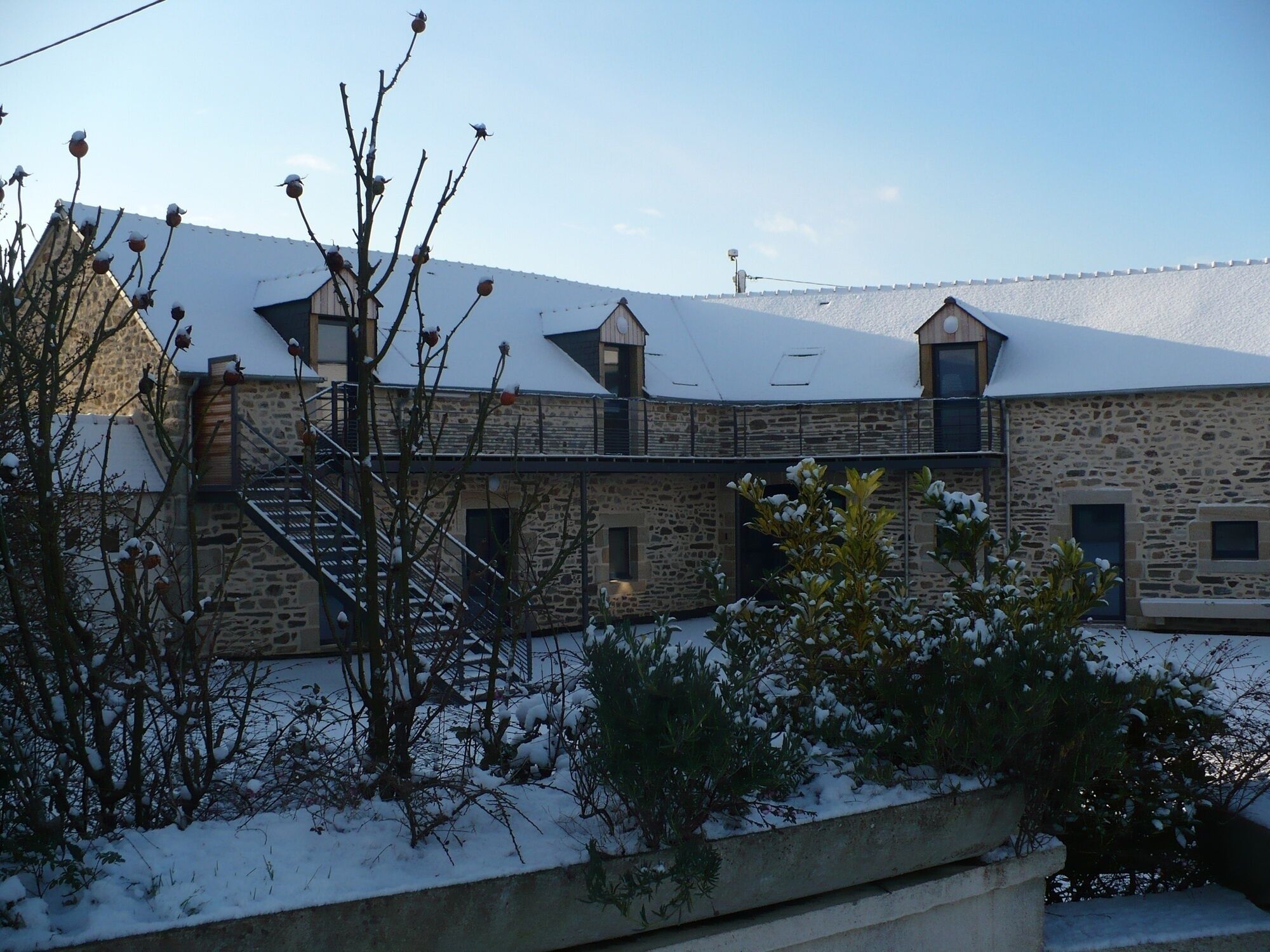 A stone building with a snow-covered roof, a staircase, and a view of the surrounding landscape.
