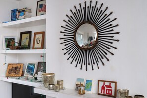 A room with a sunburst mirror, shelves with books and framed pictures, and decorative items on a mantel. - Artistic 1BDR Townhome | Central Brighton (Brighton and Hove)