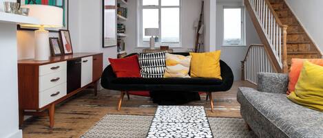 A living room with a sofa, a coffee table, a bookshelf, and a staircase.