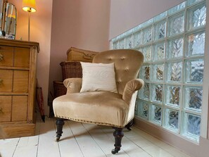 A tufted armchair with a cushion, positioned in a room with a wooden dresser and a window with decorative glass panels. - Artistic 1BDR Townhome | Central Brighton (Brighton and Hove)