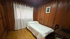 A small, single-bed room with wooden walls, a white bedspread, a wooden floor, a chair, and a curtain. - H5 Exceptional Location Near Historic Center (Popayán)