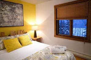 A bedroom with a bed, a window with blinds, a lamp, and a painting on the wall. - Belvedere du Lac Lodge (Sainte-Adèle)