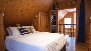 Ein Schlafzimmer einer Holzhütte mit einem Bett, einem Schminktisch und einem Fenster.
