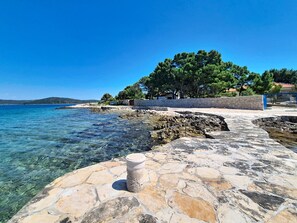 A stone pathway leading to a body of water, with a stone wall and trees in the background. - Vacation home Blue by Interhome (Drvenik Mali)