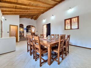 A dining area with a wooden table and chairs, a kitchen in the background, and a high ceiling with exposed beams. - Vacation home Blue by Interhome (Drvenik Mali)