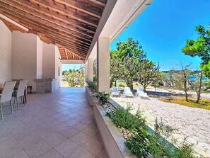 A covered patio with a tiled floor, outdoor seating, and a view of trees and landscape. - Vacation home Blue by Interhome (Drvenik Mali)