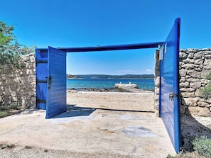 A stone wall with a blue door leading to a beach. - Vacation home Blue by Interhome (Drvenik Mali)