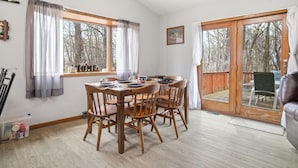 Een eethoek met een houten tafel en stoelen, een raam met gordijnen en een schuifdeur van glas die leidt naar een terras.