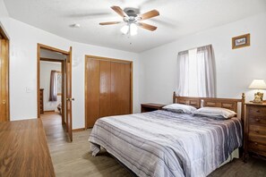 A bedroom with a bed, wooden wardrobe, ceiling fan, bedside table, and a nightstand.