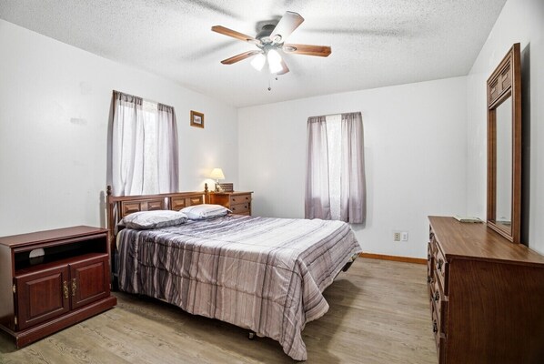 A bedroom with a bed, wooden dresser, nightstand, and a ceiling fan.