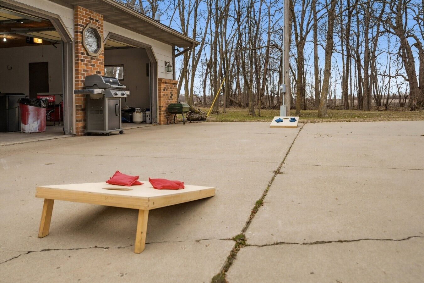Eine Beton-Terrasse mit einem Holztisch, roten Kissen, einem Grill und einer Garage mit einer Uhr.