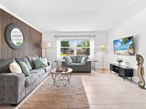 A modern living room with two grey sofas, a round coffee table, and a large window with a view of a residential area. - Baywood Colony - 2BR 2BA - Siesta Key Area (Sarasota)