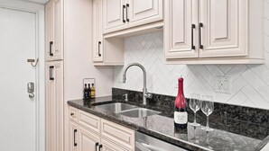 Cozinha com armários brancos, bancada de granito, pia de aço inoxidável e uma garrafa de vinho.