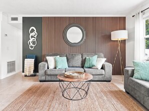 A modern living room with a grey sofa, a round coffee table, and a patterned rug. - Baywood Colony - 2BR 2BA - Siesta Key Area (Sarasota)