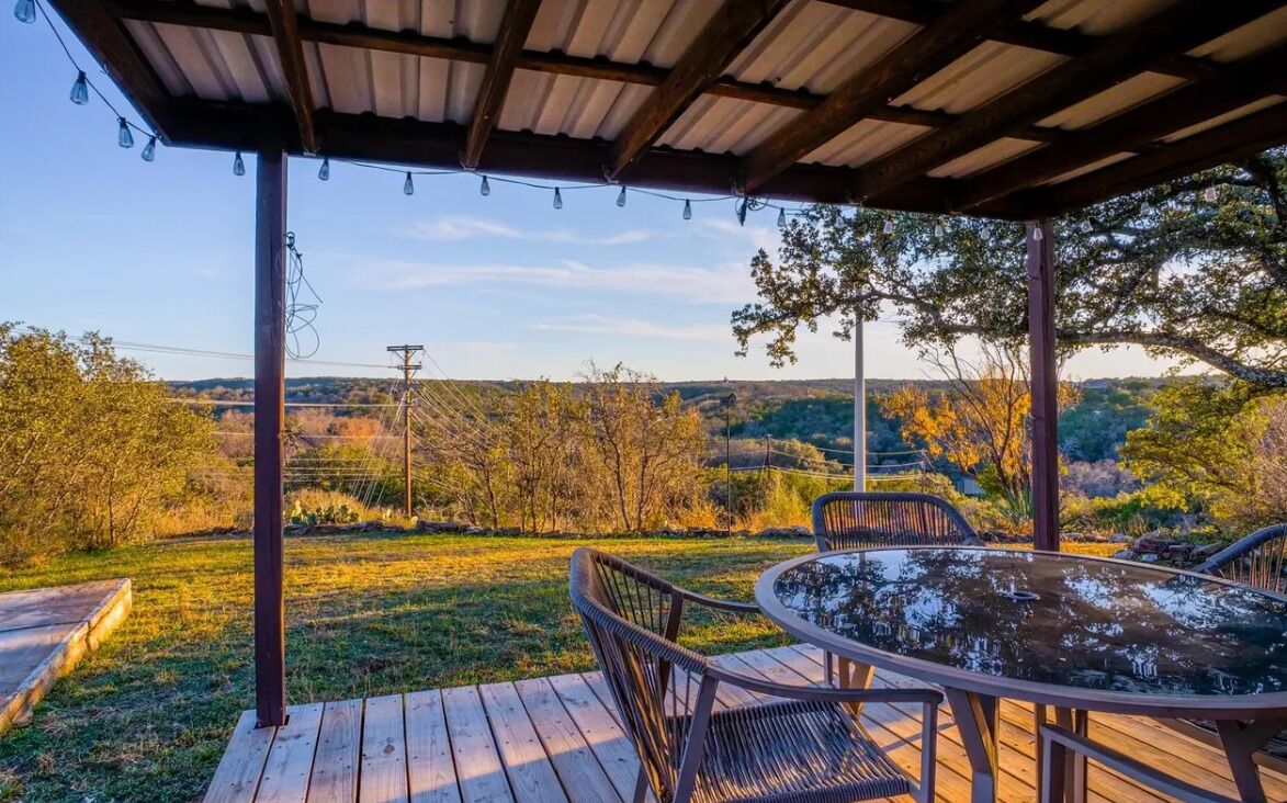 An outdoor patio with a round table and chairs, surrounded by a wooden deck and a metal pergola.