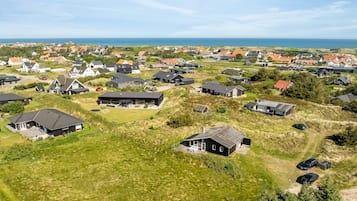 Ovenudblik over et boligområde med huse, hvoraf nogle har tilhørende garage, og et klart hav i baggrunden.