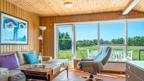 Ein Zimmer mit Holzvertäfelung, ausgestattet mit einer Couch, einem Tisch, einem Stuhl und einem großen Fenster mit Blick auf eine grüne Landschaft.