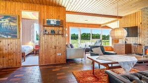 Ein modernes Interieur mit Holzwänden, einem Fischgrätparkett, einer Couch, einem Tisch und einem Kamin.