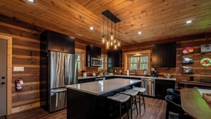 A modern kitchen with a large island, stainless steel appliances, and wooden paneling. - New Pool Cabin! Luxury Design, Game Rm, Hot Tub! (Sevierville)