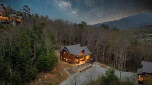 A lodge with a prominent balcony and a view of the night sky. - New Pool Cabin! Luxury Design, Game Rm, Hot Tub! (Sevierville)