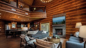 A spacious log cabin interior with a dining area, living room with sofas, fireplace, and a loft bedroom. - New Pool Cabin! Luxury Design, Game Rm, Hot Tub! (Sevierville)