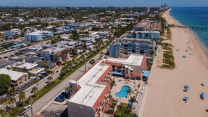 Vista aérea de una zona turística costera con playa, piscina y varios edificios hoteleros.
