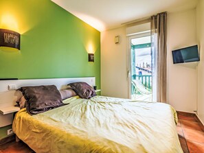 Une chambre à coucher comprenant un lit, une table de chevet, un téléviseur fixé au mur et une fenêtre donnant sur un balcon.