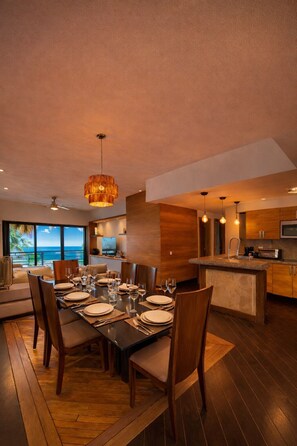 A modern dining area with a large table set for six, a kitchen with wooden cabinets, and a view of the ocean. - Prime Rooftop Pool in Aldea Thai (Playa del Carmen)