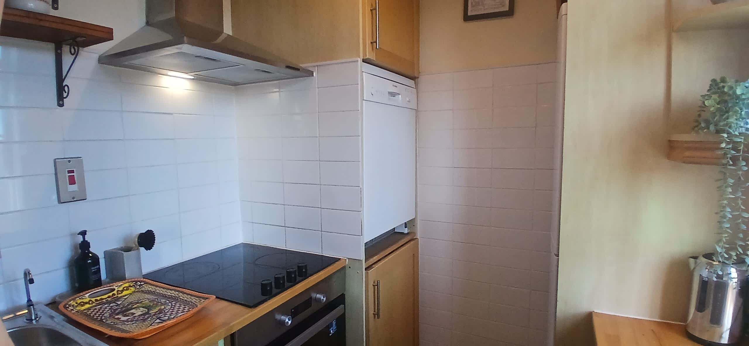 A compact kitchen with white tiles, a stove, oven, and a small countertop with a tray.