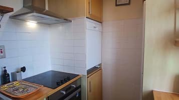 A compact kitchen with white tiles, a stove, oven, and a small countertop with a tray.