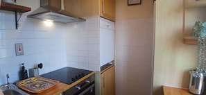 A compact kitchen with white tiles, a stove, oven, and a small countertop with a tray.