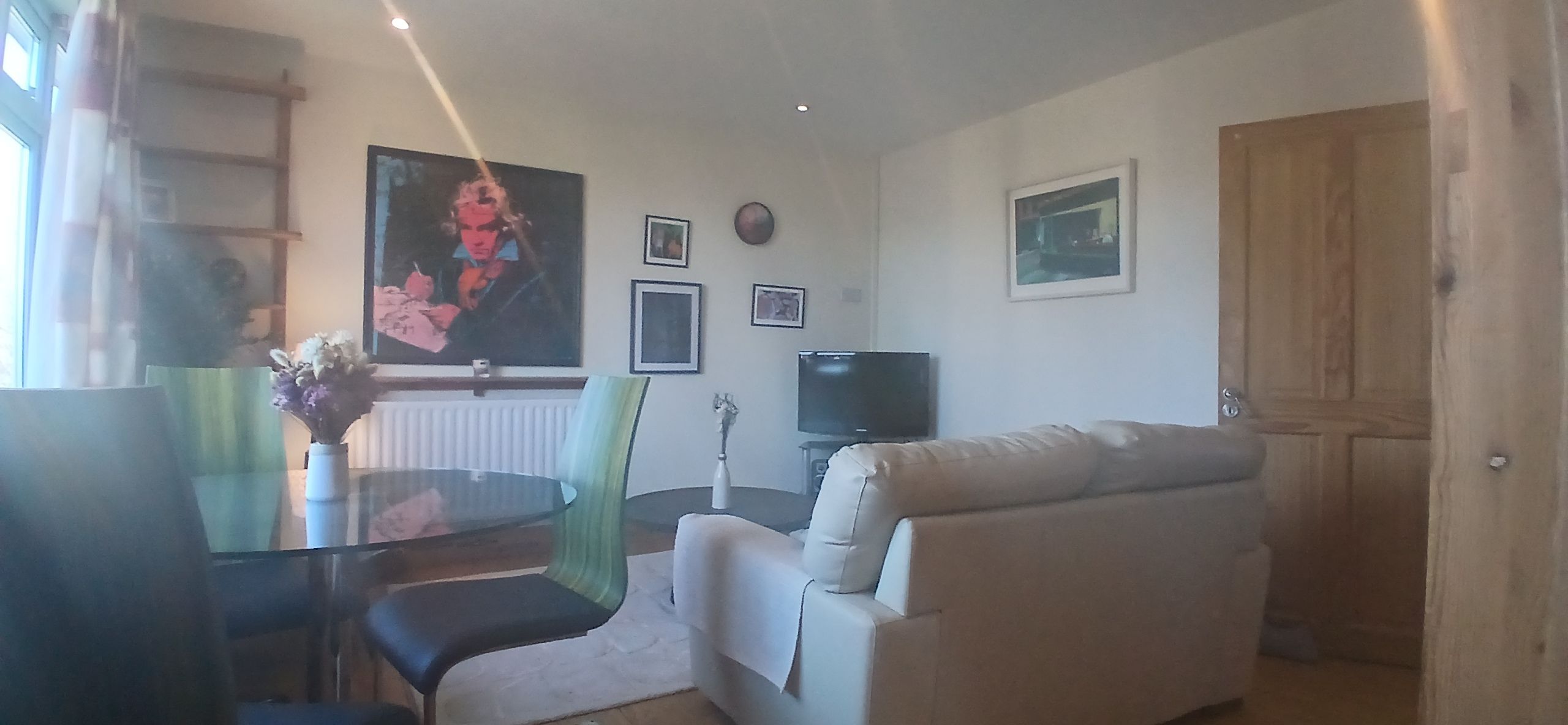 A living room with a sofa, a dining table with chairs, a TV, and framed pictures on the wall.