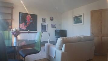 A living room with a sofa, a dining table with chairs, a TV, and framed pictures on the wall.