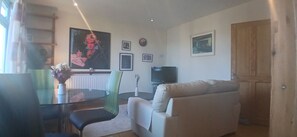 A living room with a sofa, a dining table with chairs, a TV, and framed pictures on the wall. - Bright 2BDR Sandymount Apartment Near Sea (Dublin)