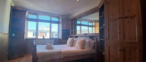 A bedroom with a bed, a wooden wardrobe, and a window with blinds.