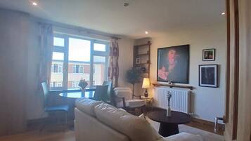 A living room with a sofa, a round table, a lamp, a TV, and a window with curtains.