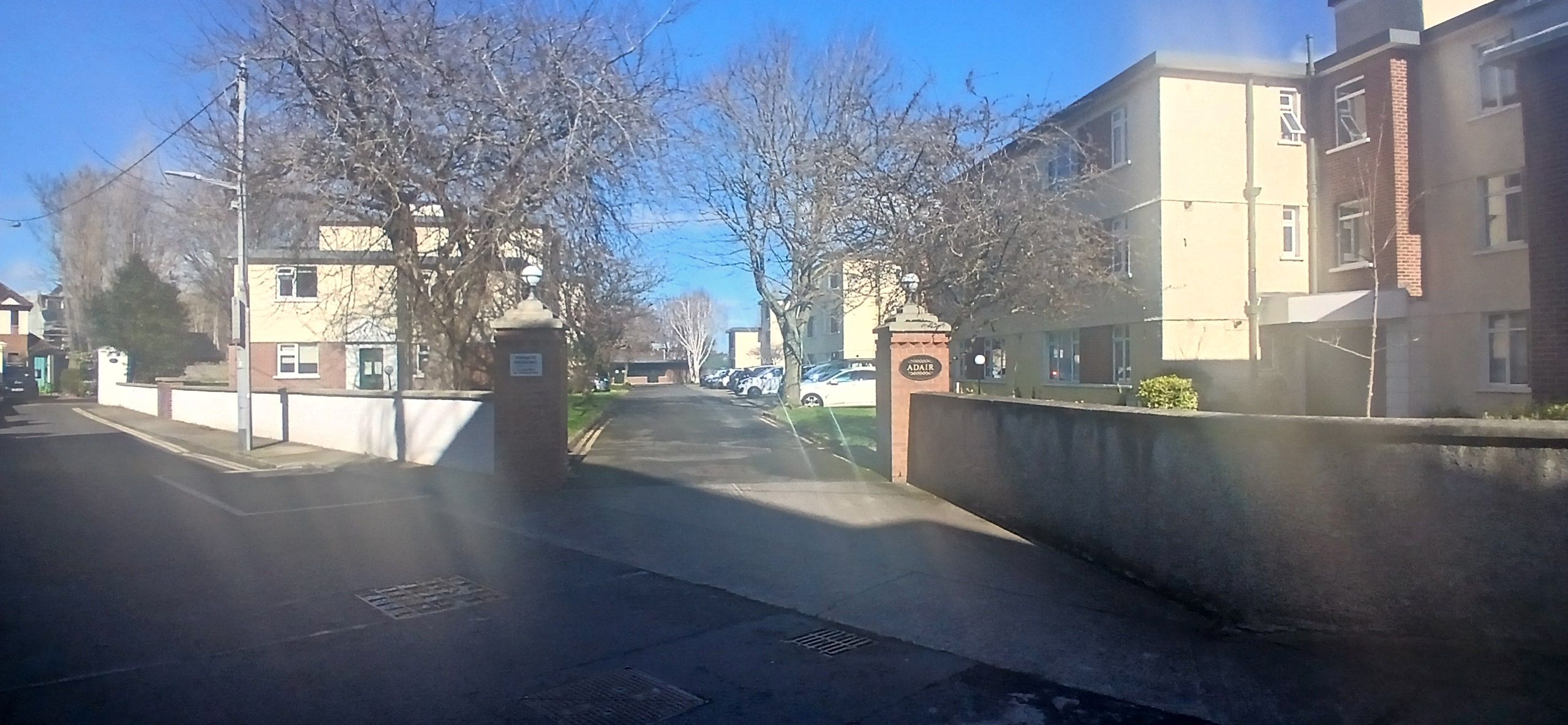 A residential street with a gated entrance, a clear sky, and buildings on either side.