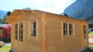 A wooden cabin with a gabled roof, large windows, and a flat roof extension.