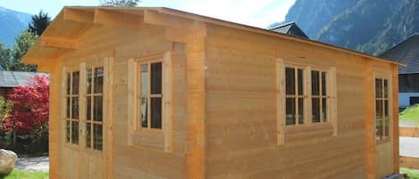 A wooden cabin with a gabled roof, large windows, and a flat roof extension.
