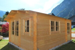 Una cabaña de madera con techo a dos aguas, ventanas amplias y un porche techado.