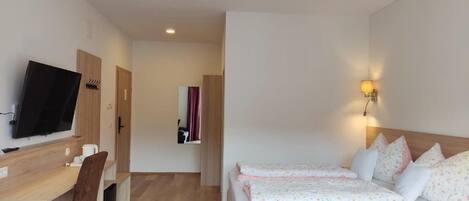 A hotel room with a TV, a desk, two beds, and a hallway leading to another room.