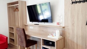 A modern room with a wooden desk, a television, a chair, a red sofa, and a coat rack.
