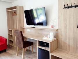 Una habitación moderna con un escritorio de madera, televisor, silla, sofá rojo y perchero.