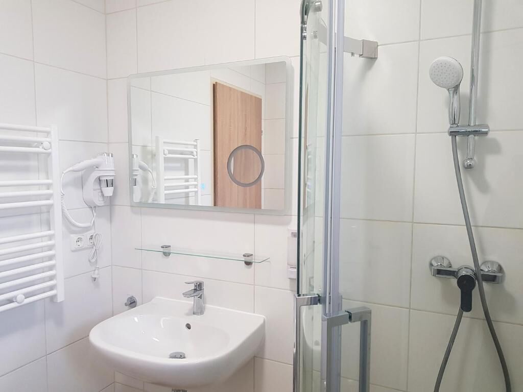 Een badkamer met een witte wastafel, een douchecabine van glas en een spiegel boven de wastafel.
