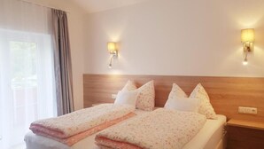 A double bed with a wooden headboard, two wall-mounted lamps, and a window with curtains.