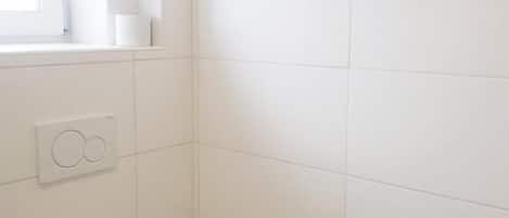 A small, white bathroom with a toilet, a window, and a paper towel dispenser.