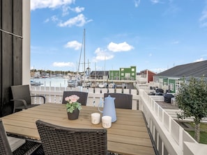 A wooden deck with outdoor seating, a view of a marina with boats, and a green building in the background. - "Björk" - 10m from the sea by Interhome (Ebeltoft)
