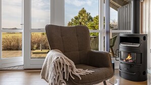 Ein gemütliches Zimmer mit großem Fenster, bequemen Sessel und Kaminofen.