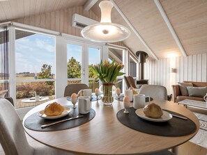 En matplats med ett bord dukat för frukost, en öppen spis och stora fönster med utsikt över omgivningarna.