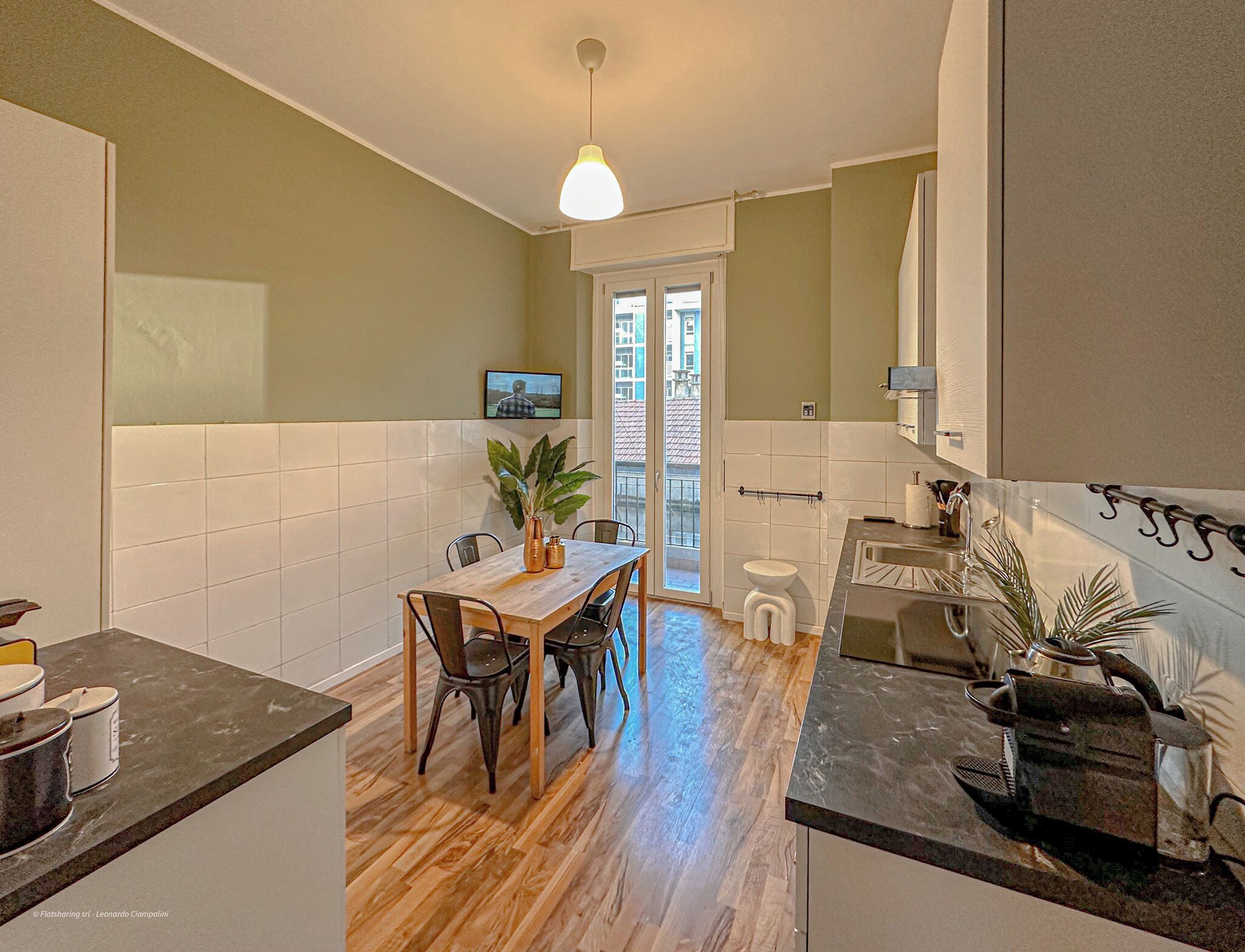 Una cocina con comedor, piso de madera, televisor y vistas al exterior.